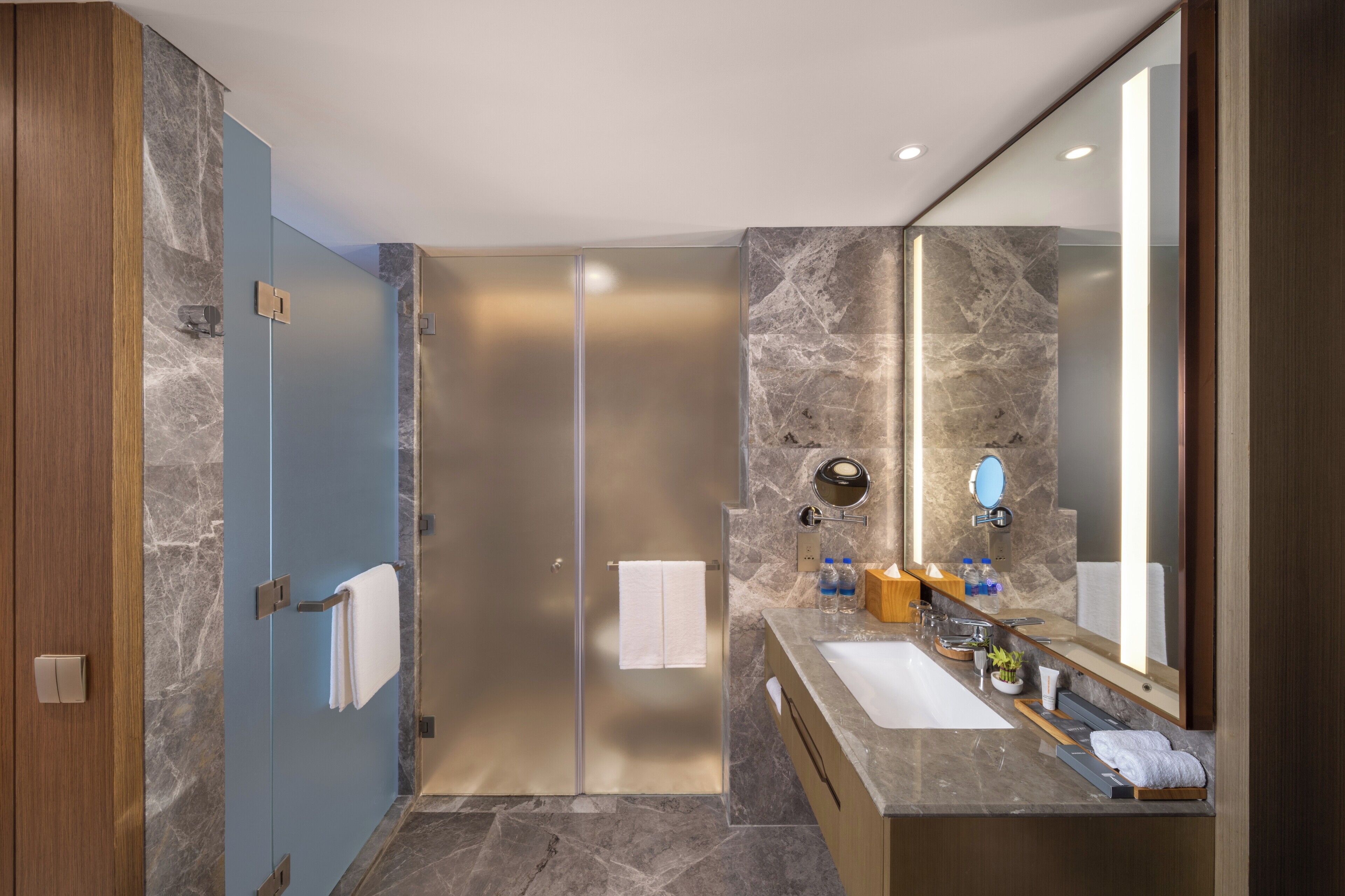 A modern bathroom with a glass shower door, a large mirror, and a marble countertop.