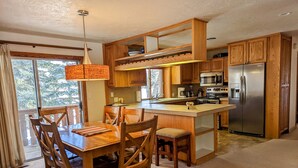A modern kitchen with wooden cabinets, a stainless steel refrigerator, and a dining area with wooden chairs and a table.