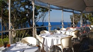 Un espace extérieur aménagé pour les repas, avec des tables et des chaises, donnant sur un plan d’eau.