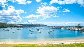 Un port de plaisance où sont amarrés de nombreux bateaux, une plage de sable au premier plan et un ciel bleu clair parsemé de quelques nuages.