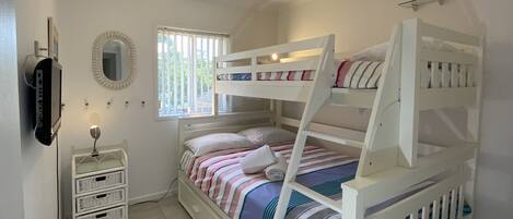 Une chambre avec un lit superposé, un ventilateur de plafond, un miroir et une fenêtre avec des stores.