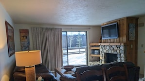 Una sala de estar acogedora con una chimenea de piedra, un televisor montado encima y un sofá cómodo, además de una mesa con una lámpara.