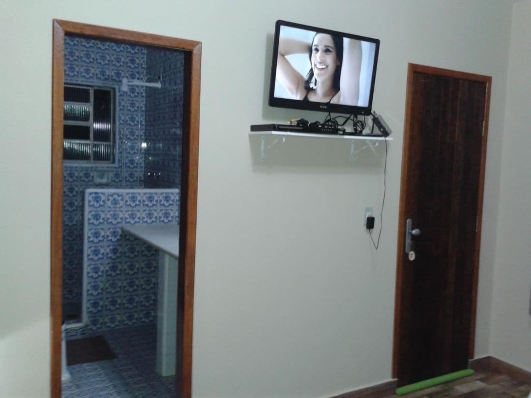 Quarto com televisão em prateleira fixada na parede, porta de madeira e parede com azulejos estampados.