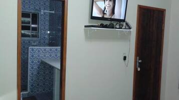 Quarto com televisão em prateleira fixada na parede, porta de madeira e parede com azulejos estampados.