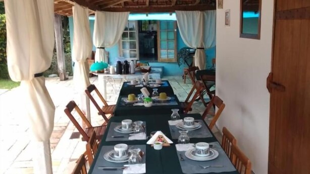 An outdoor dining area with a long table set for a meal, covered with a dark tablecloth. - Acomodação Penedo (Itatiaia)