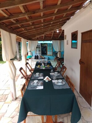 Un área de comedor al aire libre con una mesa larga preparada para una comida, cubierta con un mantel oscuro.