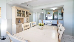 A dining area with a white table and chairs, a cabinet with glass doors, and a kitchen in the background. - CRC 3305 - Third Floor Ocean View Condo (St Augustine)