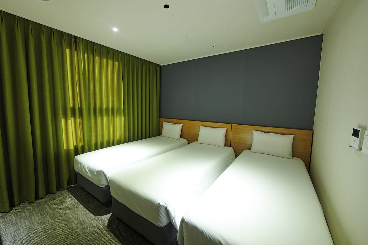 Habitación de hotel con dos camas, cabecera de madera, cortina verde y piso alfombrado.
