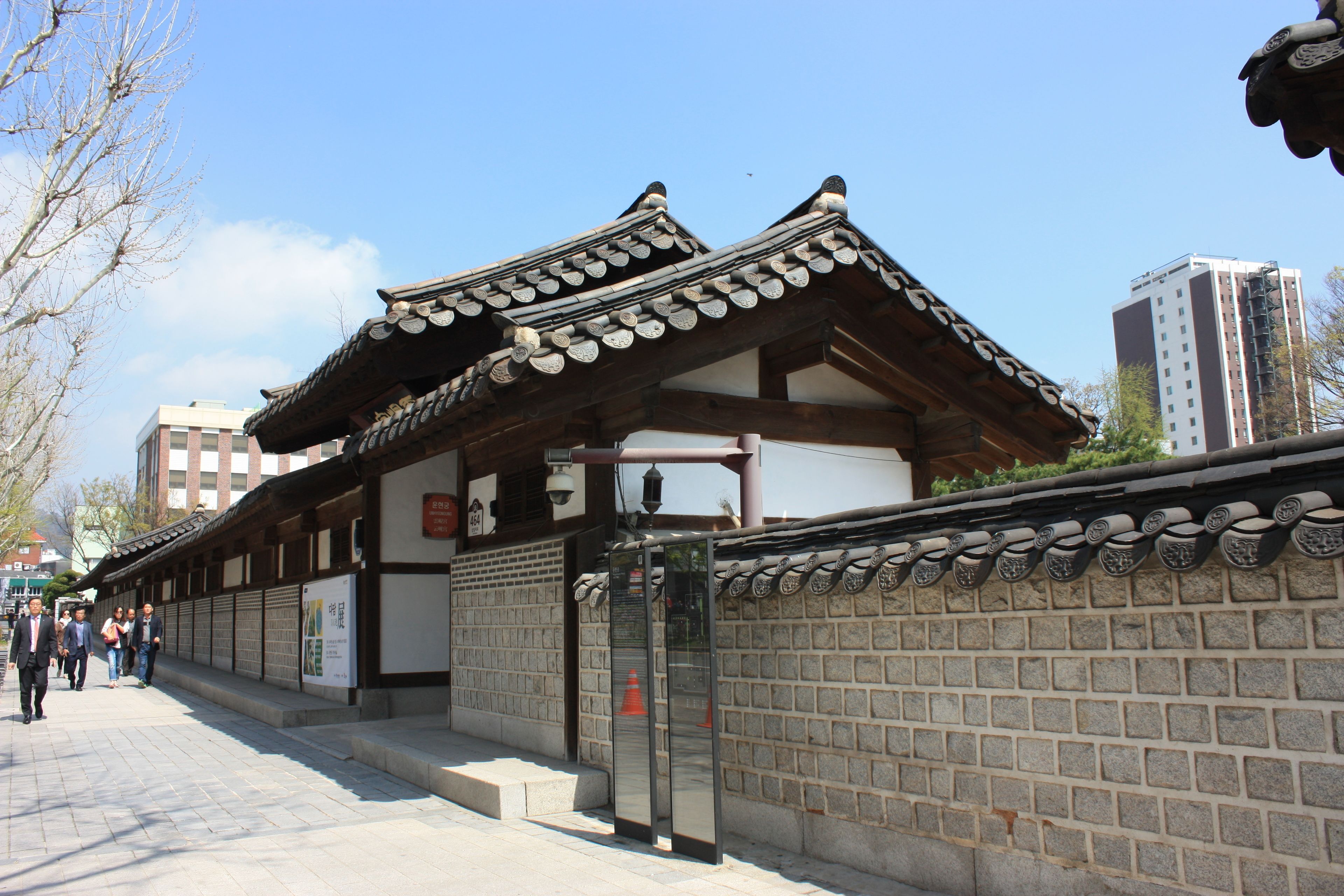 A traditional building with a tiled roof and wooden beams, a brick wall with decorative elements, and a clear sky.