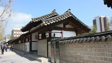 A traditional building with a tiled roof and wooden beams, a brick wall with decorative elements, and a clear sky.