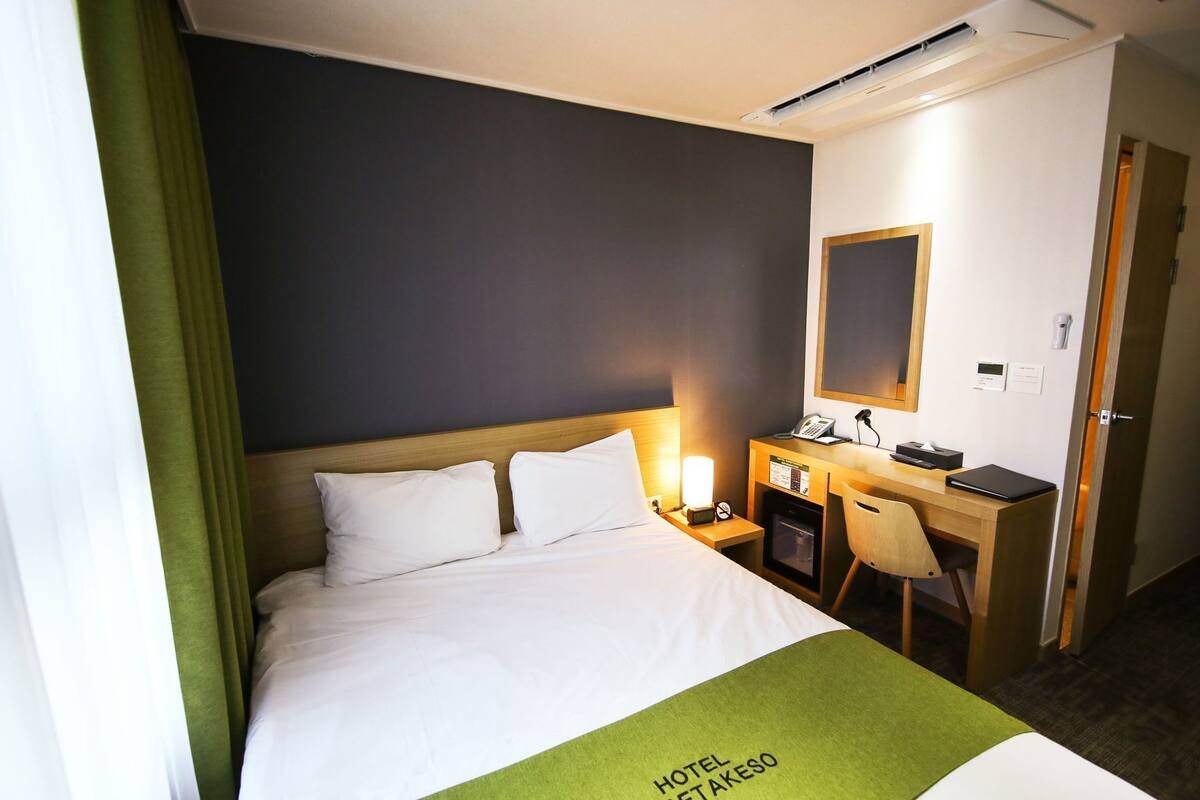 Habitación de hotel con cama, escritorio, silla, teléfono y un refrigerador pequeño.