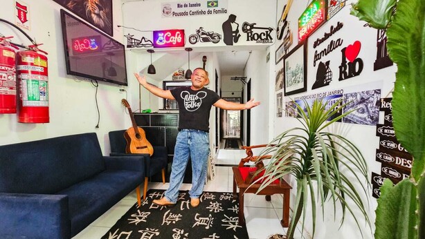 A room with a blue sofa, a guitar, a neon sign, and various posters on the walls. - Pousada Cantinho da Familia (Rio de Janeiro)