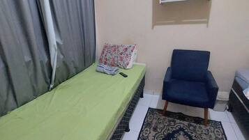 Una habitación pequeña y sencilla con cama, una silla, un tapete y un equipo de aire acondicionado en la pared.
