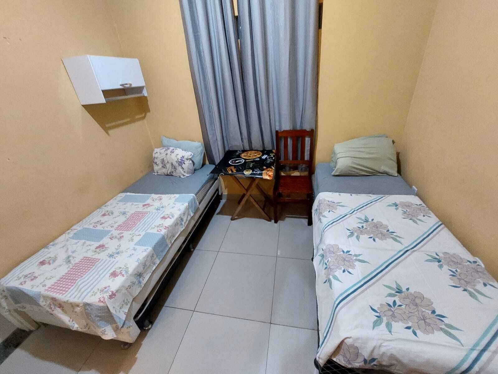 A small, compact room with two single beds, a small table with a chair, and a window with curtains.