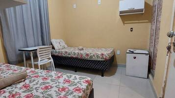 A small, well-lit room with two beds, a table, chairs, and a refrigerator.