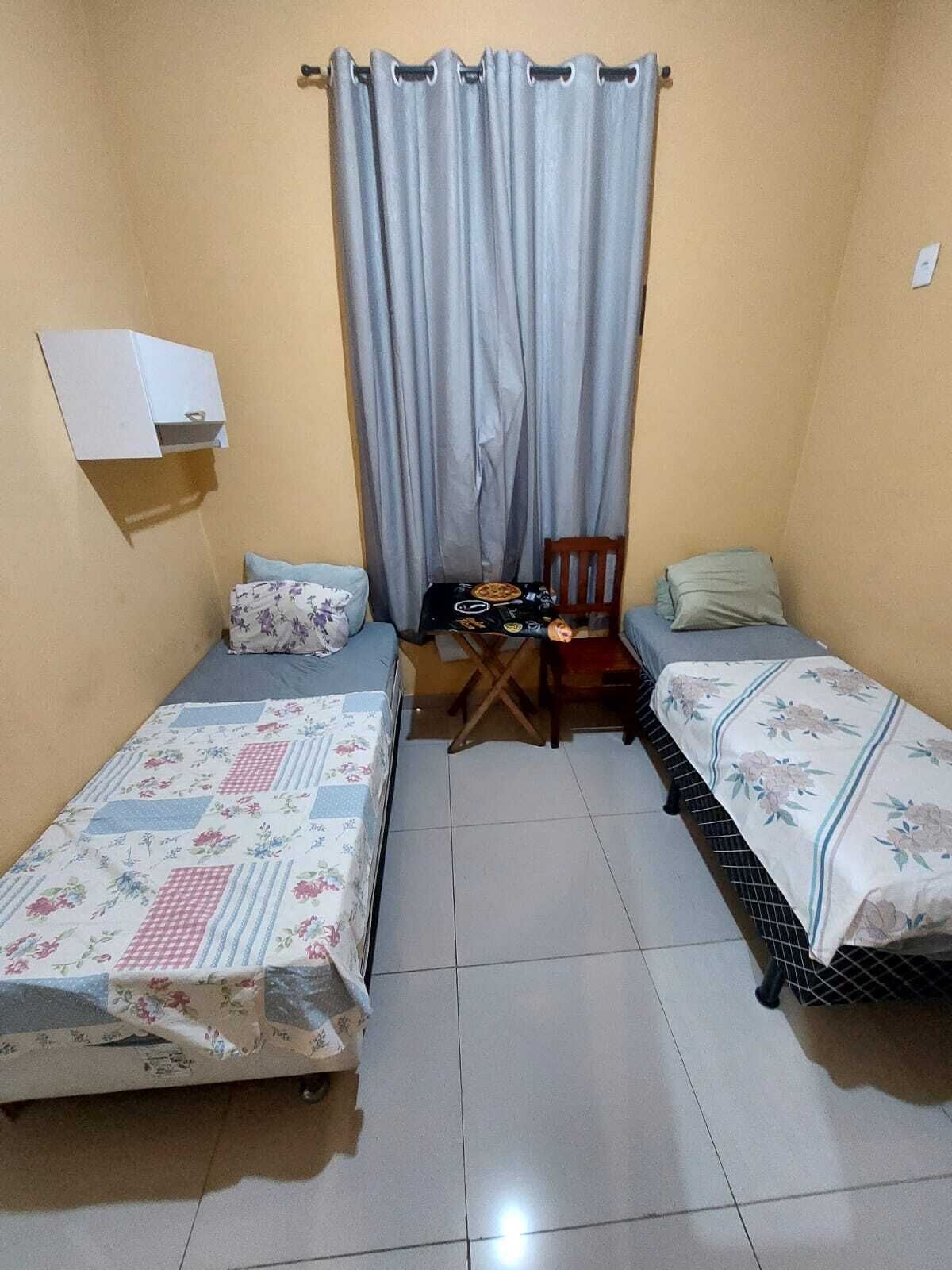 Een kleine, compacte kamer met twee eenpersoonsbedden, een tafeltje en een stoel.