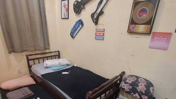 Ein kleines Zimmer mit einem Einzelbett, einem Holzkopfteil, einem stuhl mit Blumenmuster und verschiedenen Wanddekorationen, darunter Gitarren und eine Schallplatte.