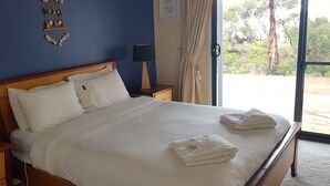 Een net opgemaakt bed met witte lakens en handdoeken, een houten hoofdbord, nachtlampjes en een decoratief wandobject.