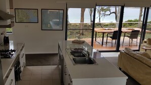 Een moderne keuken met een groot schiereiland, een eetgedeelte met uitzicht op de oceaan, en een gezellige zithoek met uitzicht op het terras.