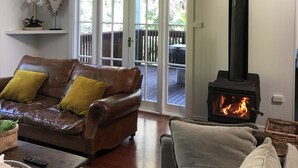 A cozy living room with a leather sofa, a fireplace, and a large arched doorway leading to an outdoor deck. - Luxurious Jetty House, Coffs Harbour – privacy & tranquility (Coffs Harbour)