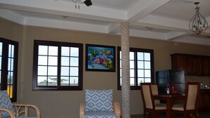 Amplia sala de estar con ventanas grandes, una mesa de comedor y una cocina al fondo.