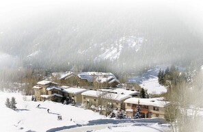 Un complejo turístico nevado con varios edificios, pistas de esquí y montañas al fondo.