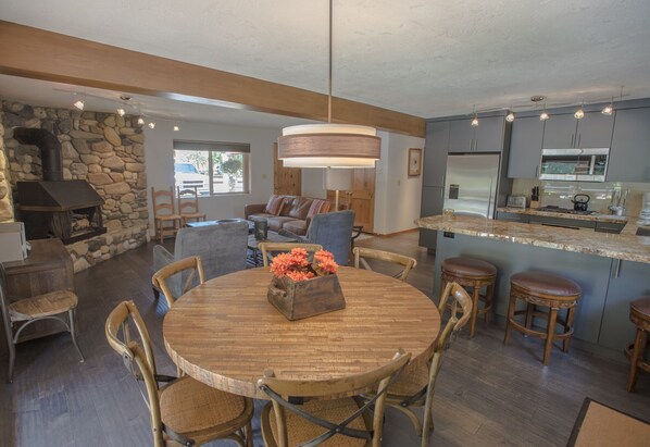 Una cocina amplia con chimenea de piedra, una mesa de comedor de madera y taburetes de bar.