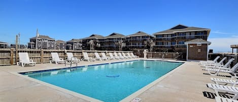 A rectangular swimming pool with lounge chairs and a wooden fence.