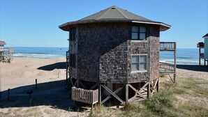 Una casa de playa con fachada de madera, un balcón y vista al océano.