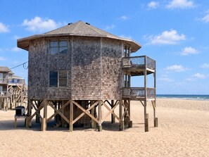 Une tour de surveillance en bois, dotée d’un balcon, se dresse sur une plage de sable.