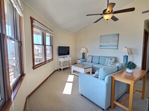 Ein Wohnzimmer mit einer Couch, einem Couchtisch, einem Fernseher und einem Deckenventilator.