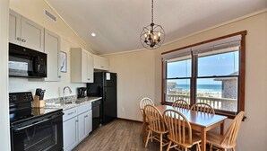 Una cocina con armarios blancos, un microondas negro y una mesa de comedor de madera con sillas.