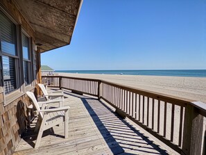 Eine Holzterrasse mit Stühlen, einem Geländer und Blick auf Strand und Meer.