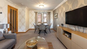 Een woonkamer met een bank, een eettafel met stoelen, een televisie en een open haard.