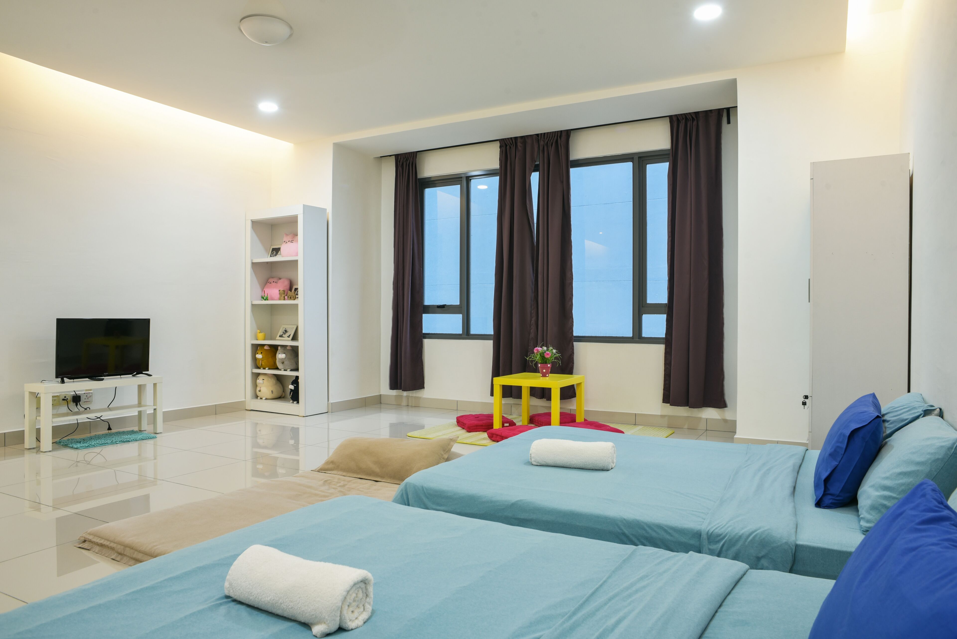 Habitación de hotel moderna con dos camas, un televisor, una mesita con una planta y una ventana con cortinas.