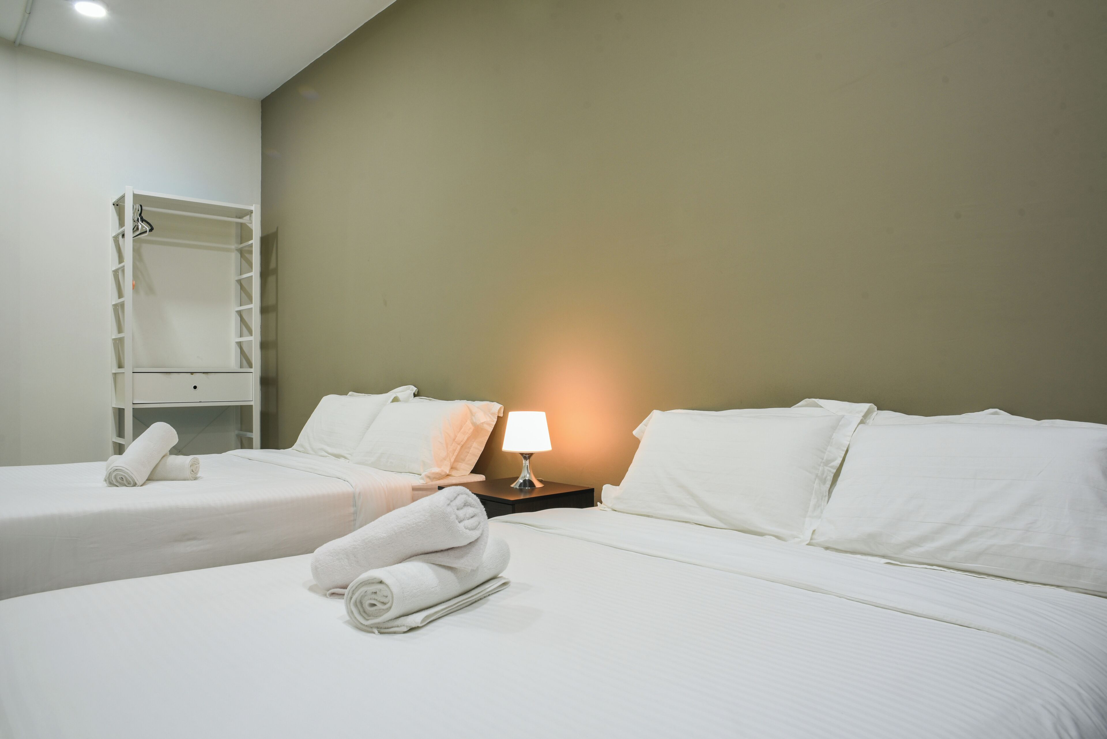 Habitación de hotel con dos camas, un armario y una mesita de noche con lámpara.
