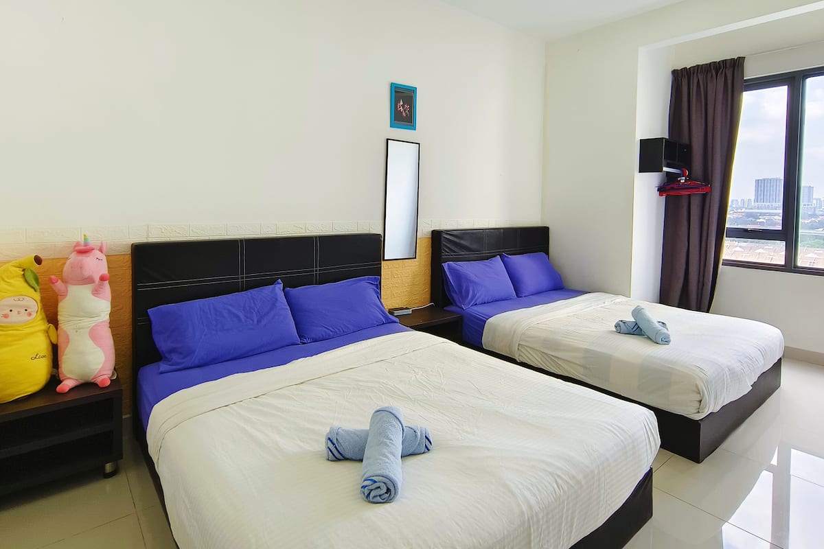 Habitación de hotel con dos camas, cada una con ropa de cama azul y blanca, y vista a la ciudad desde la ventana.