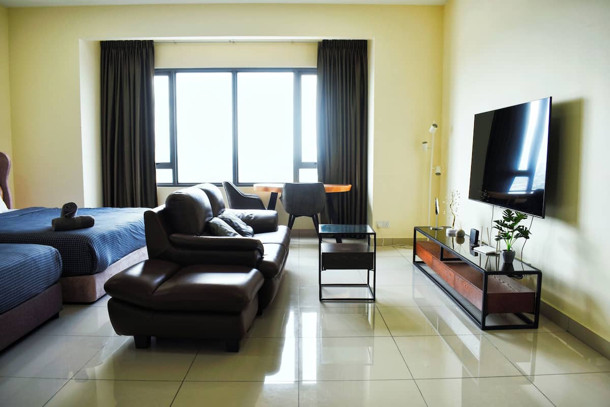Una habitación de hotel con cama, sofá, televisión y ventana con cortinas.