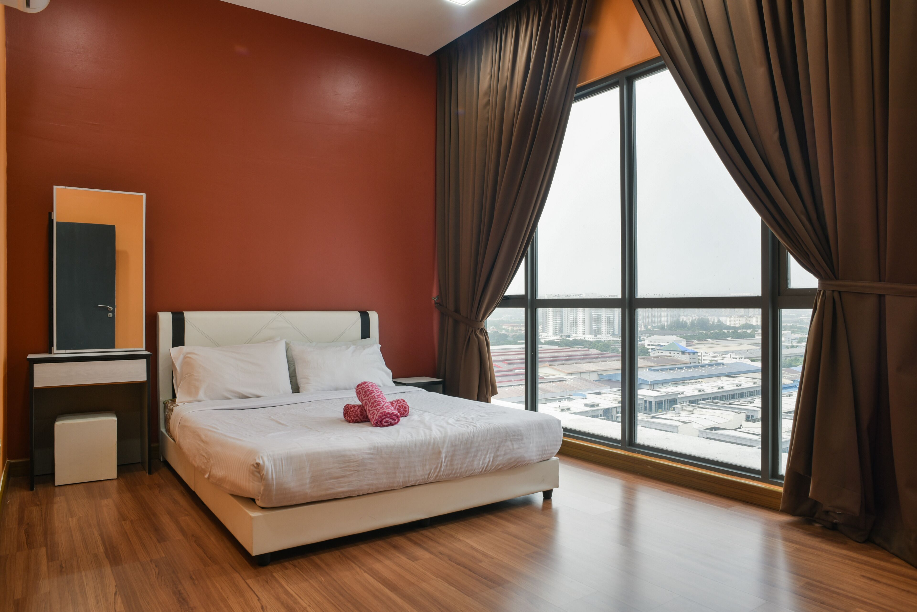 A hotel room with a large window, a bed, a desk, and a wardrobe.
