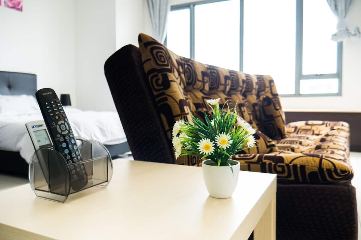 Habitación de hotel con cama, sofá, un atril para el control remoto y un florero con flores.