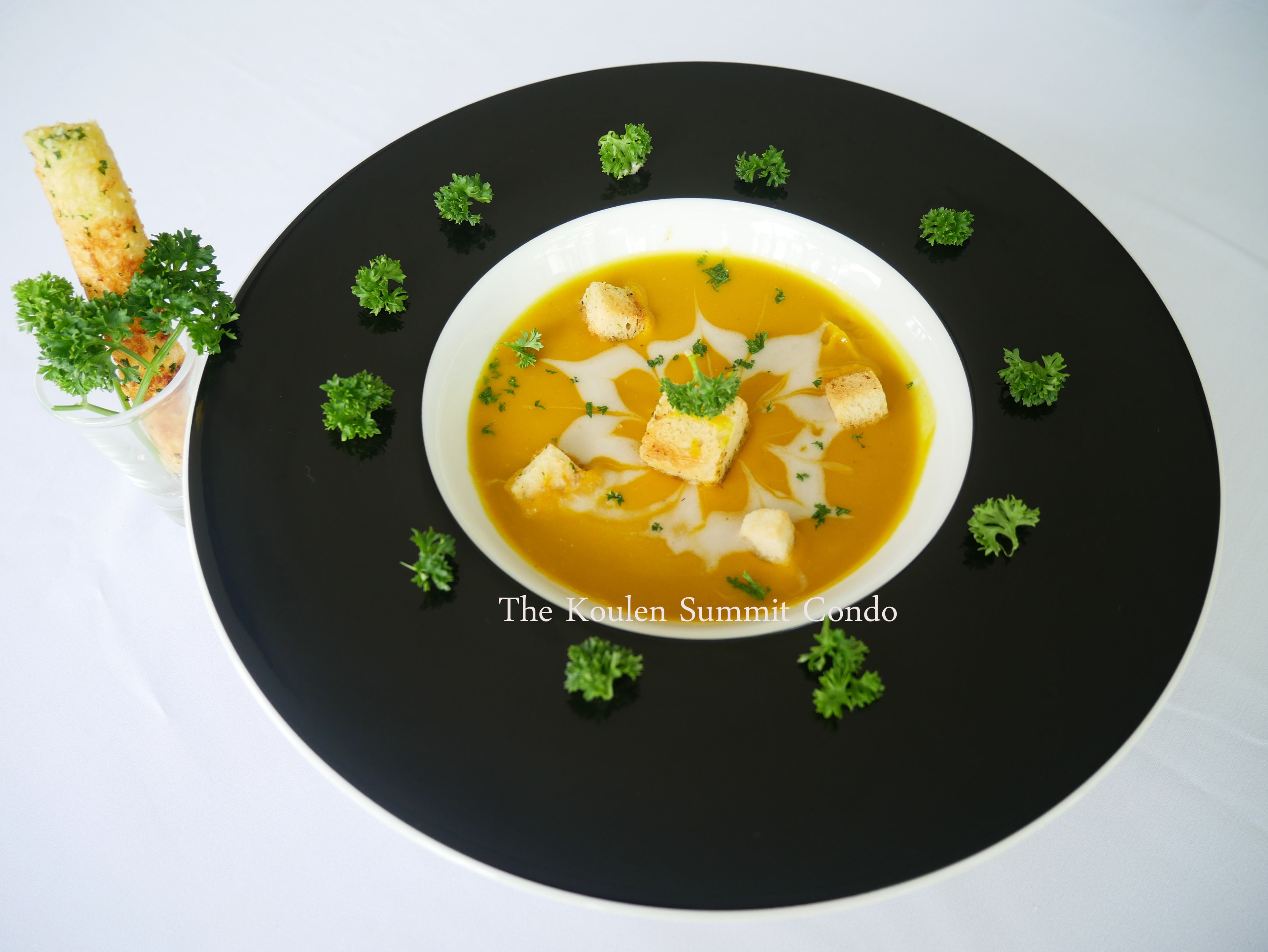 Un tazón de sopa con crutones y perejil sobre un plato negro.