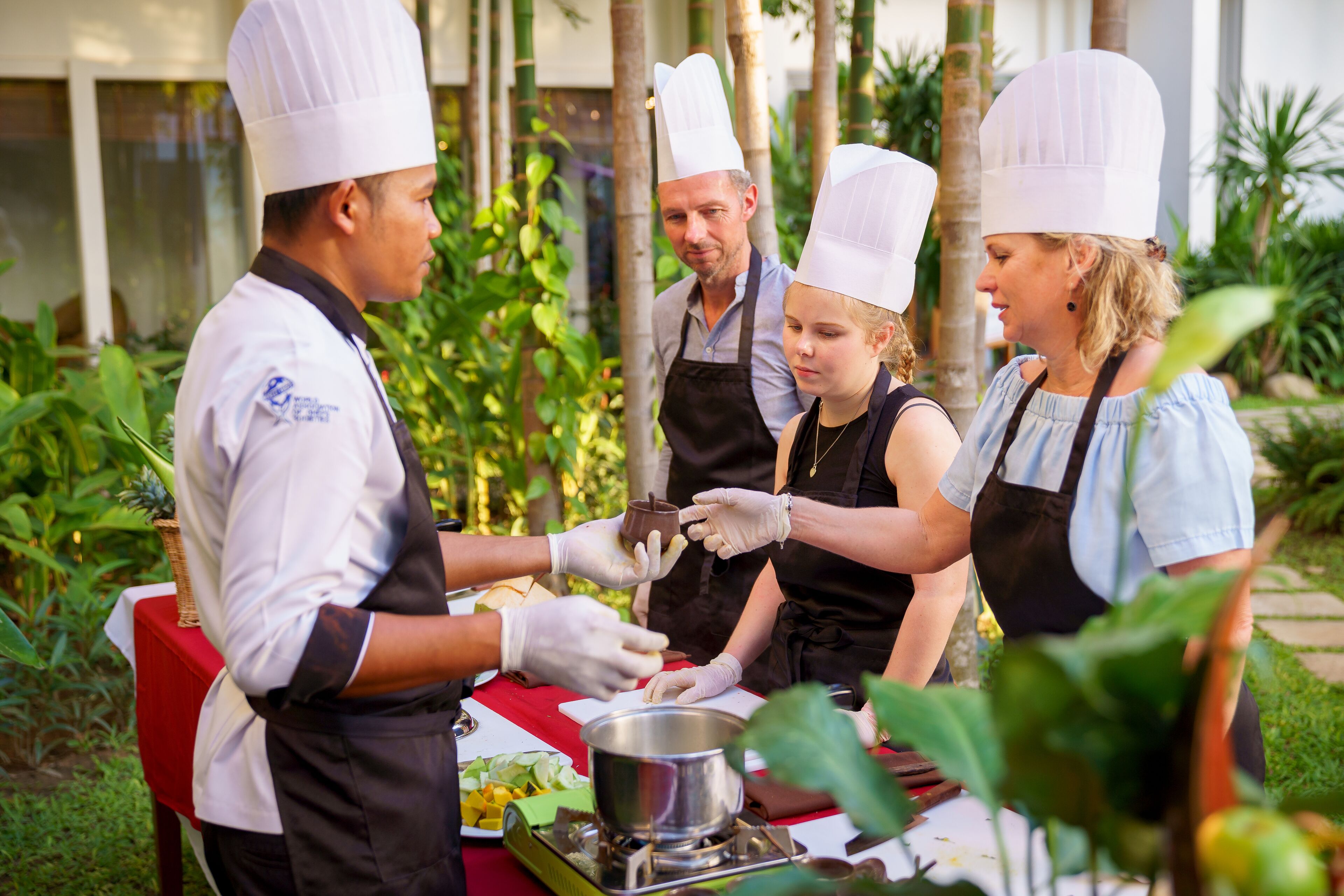 Un groupe de chefs, coiffés de toques blanches et portant des tabliers, prépare des plats en plein air.