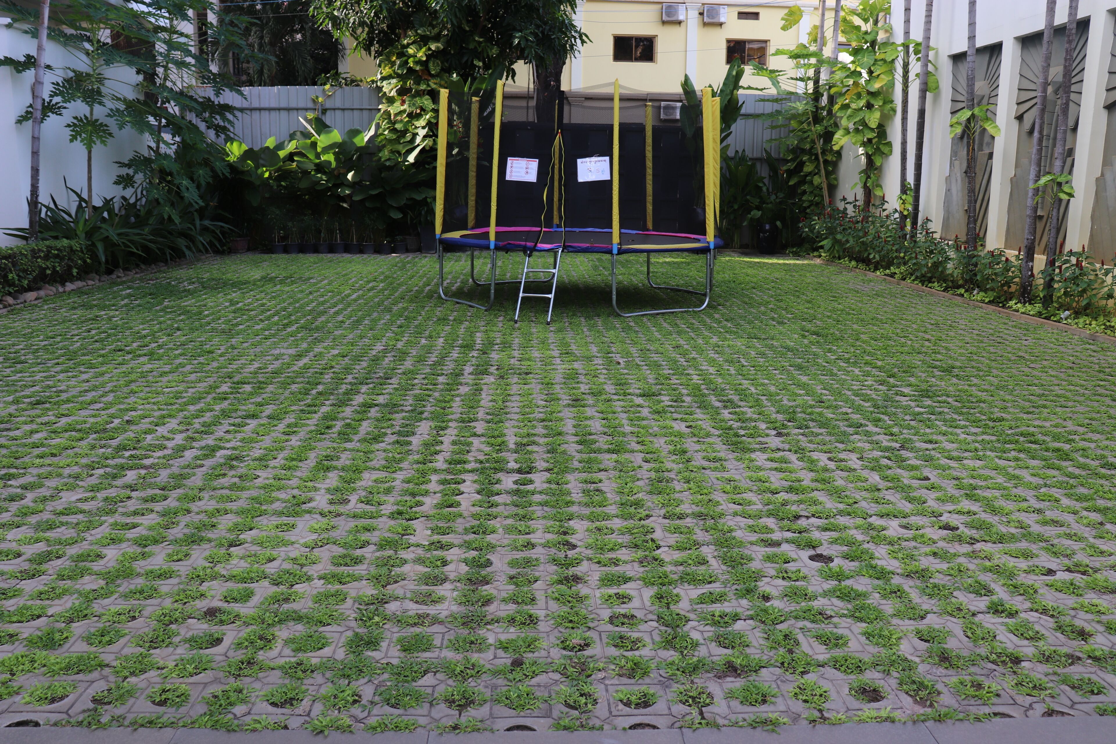 Un trampolín en un jardín con suelo empedrado.