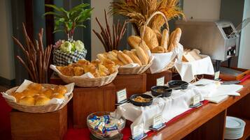 Uma mesa de buffet com pães, doces e acompanhamentos variados.