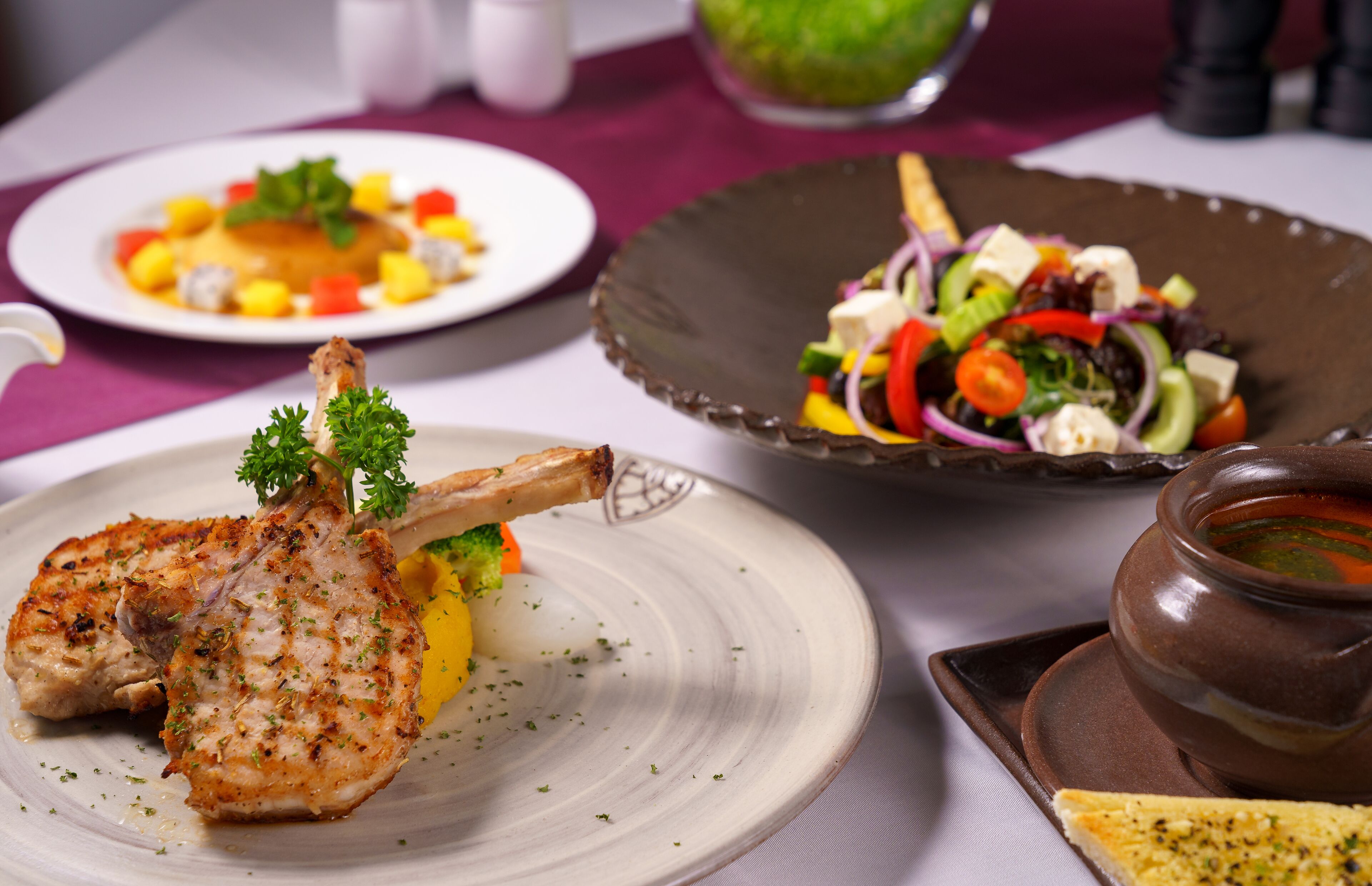 A dining table with plates of food, including a lamb shank, a salad, and a bowl of soup.
