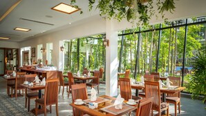 A restaurant with wooden tables and chairs, large windows, and hanging plants.