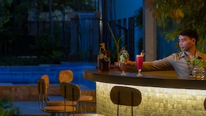 An outdoor bar area with a thatched roof, hanging lights, and a stone wall.