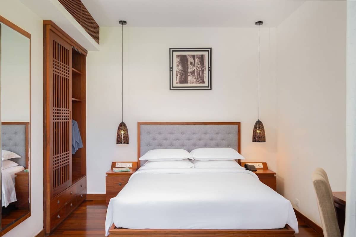 A neatly arranged bedroom with a large bed, wooden wardrobe, and two bedside tables with lamps.