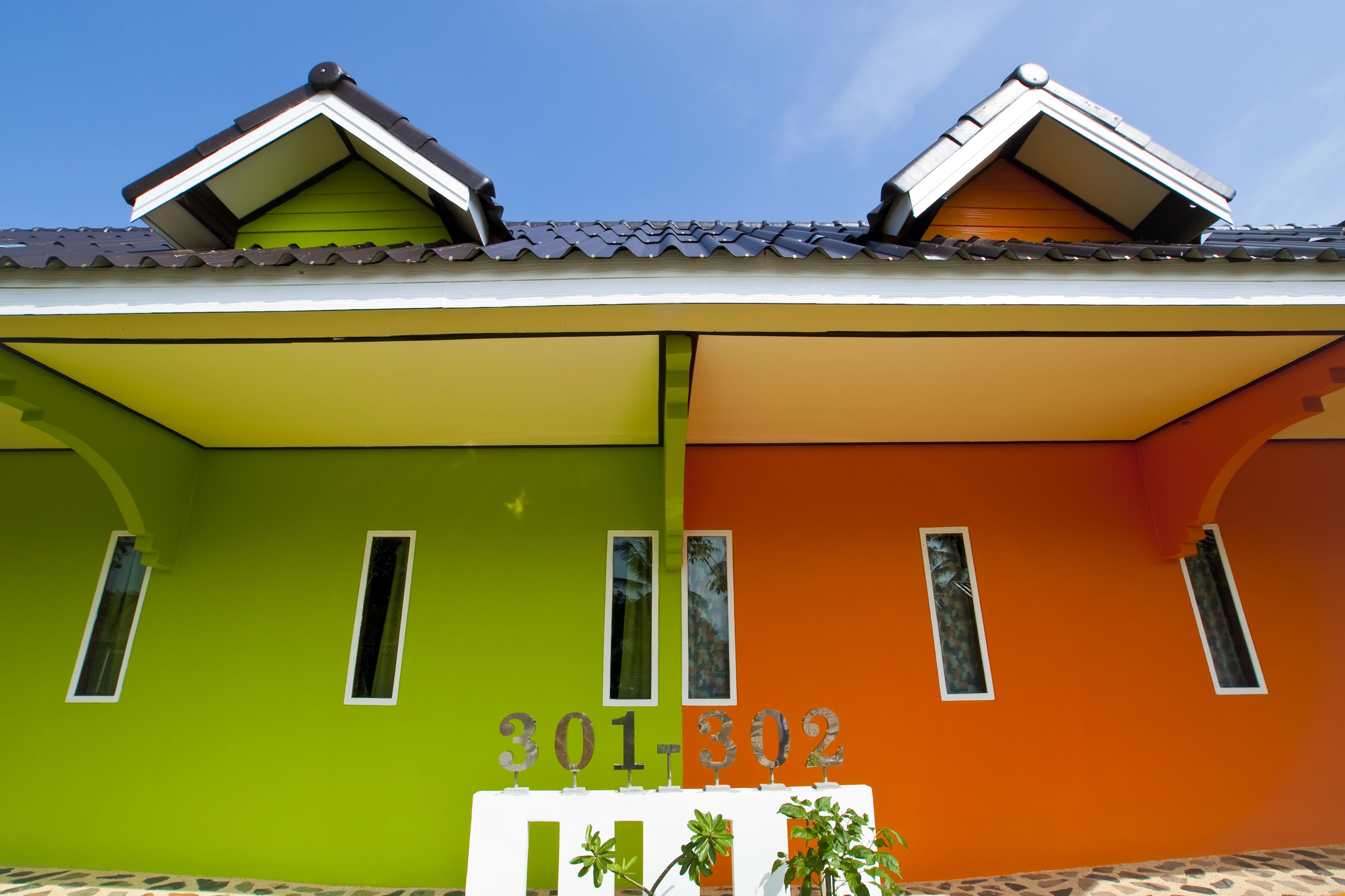 Un bâtiment aux couleurs vives, avec une façade verte et orange, des fenêtres numérotées et un toit recouvert de tuiles.