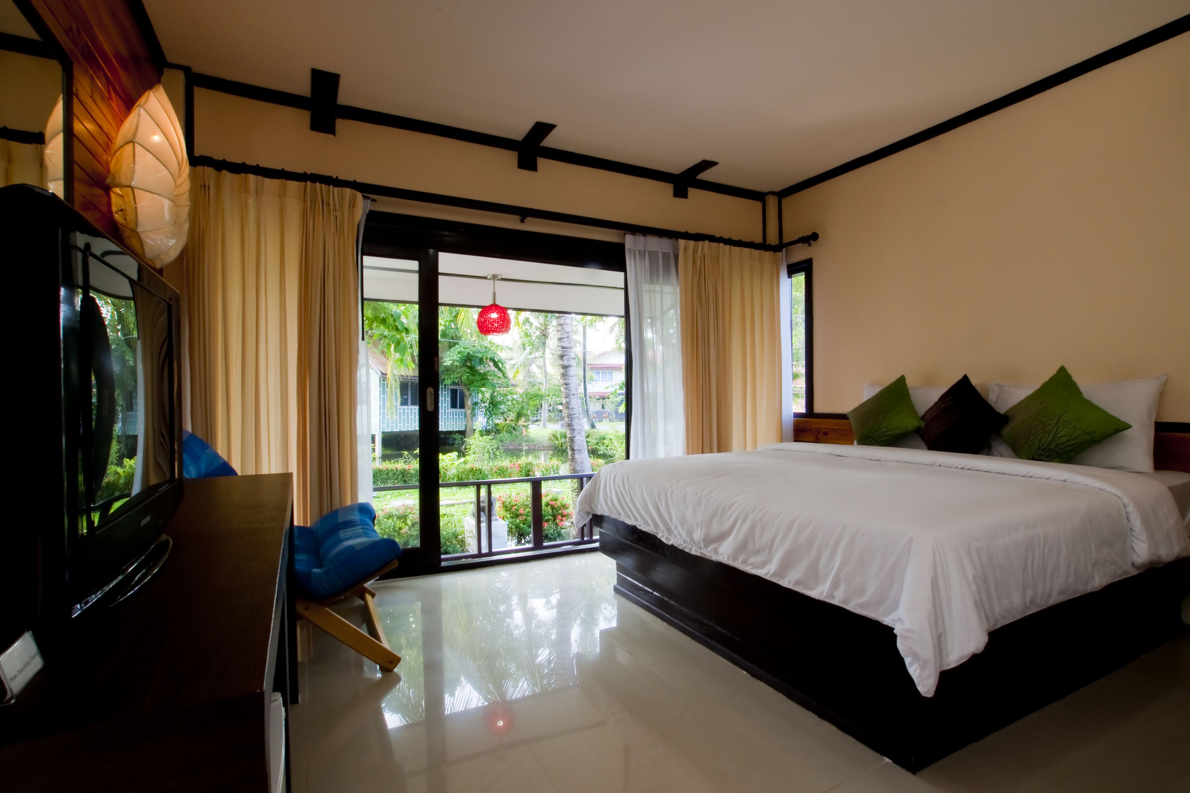 A hotel room with a large bed, a TV, and a balcony with curtains.